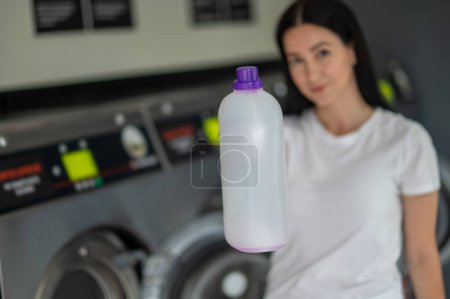 Photo for Young woman holding detergent using washing machine in public laundry. - Royalty Free Image