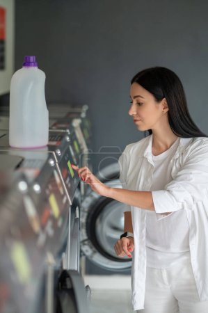 Photo for Young woman turning washingmachine in public laundry room. - Royalty Free Image