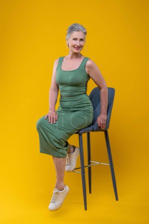 Téléchargez les photos : Femme en vert. Femme âgée aux cheveux gris en vert assise sur la chaise - en image libre de droit