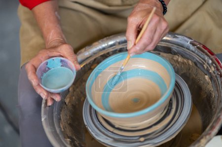 Photo for Closeup of woman painting clay mug, coloring pottery in workshop with a paintbrush. Painter glazing clay pot. - Royalty Free Image