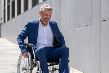 Foto de Hombre de pelo gris guapo discapacitado que usa traje formal en silla de ruedas al aire libre. - Imagen libre de derechos