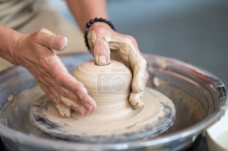 Photo for Unrecognizable woman working on potters wheel in a pottery workshop, creating clay pot. - Royalty Free Image