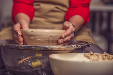 Foto de Mujer alfarera irreconocible creando hermoso plato con arcilla, haciendo obras de arte con sus manos. - Imagen libre de derechos