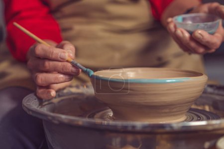 Foto de Primer plano de la mujer pintando taza de arcilla, cerámica para colorear en el taller con un pincel. Pintor vidriera olla de arcilla. - Imagen libre de derechos