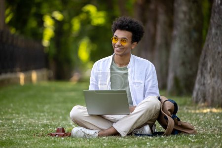 Photo for Digital nomad. Young curly-haired man working on laptop in the park - Royalty Free Image