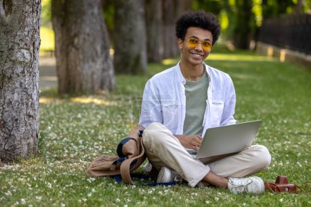 Photo for Working remotely. Man in light clothes sitting on the grass and working on laptop - Royalty Free Image