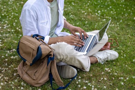 Photo for Working remotely. Man in light clothes sitting on the grass and working on laptop - Royalty Free Image