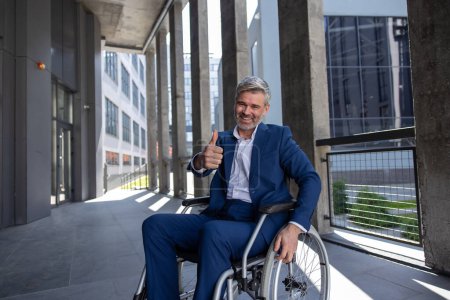 Photo for Joyful gray haired disabled man wearing official style suit in wheelchair showing thumb up like gesture. - Royalty Free Image