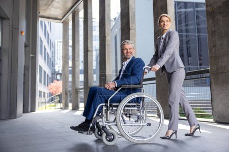 Photo for Blonde woman assisting man business partner in wheelchair going to office. - Royalty Free Image
