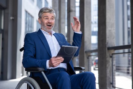 Téléchargez les photos : Homme d'affaires inspiré en fauteuil roulant avec tablette PC dans les mains, navigation sur le web, en utilisant un appareil mobile pour travailler à l'extérieur, avoir une nouvelle idée de projet. - en image libre de droit