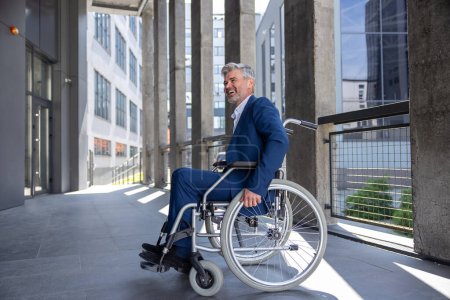 Téléchargez les photos : Homme handicapé aux cheveux gris souriant portant un costume de style officiel en fauteuil roulant fond de ville. - en image libre de droit