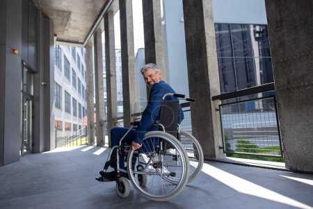 Foto de Sonriente hombre discapacitado gris con traje de estilo oficial en el fondo de la ciudad silla de ruedas. - Imagen libre de derechos