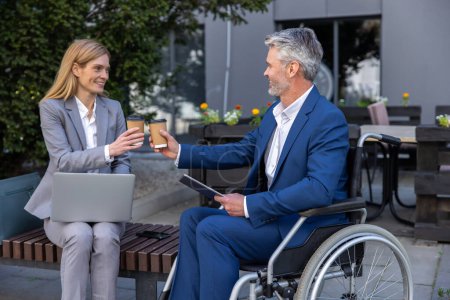 Photo for People having meeting in outdoor cafe, businessman in wheelchair and female partner talking and drinking coffee together. - Royalty Free Image