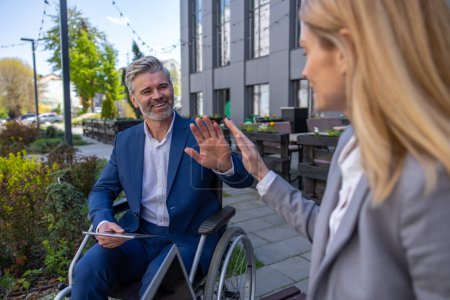 Téléchargez les photos : Sourire femme positive et l'homme en fauteuil roulant saluant les mains en disant au revoir après la réunion de bussins - en image libre de droit