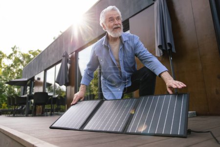 Photo for Gray haired mature man with solar panel on house porch. - Royalty Free Image