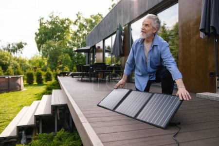 Photo for Gray haired mature man with solar panel on house porch. - Royalty Free Image