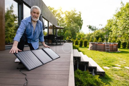Foto de Hombre maduro de pelo gris con panel solar en el porche de la casa. - Imagen libre de derechos