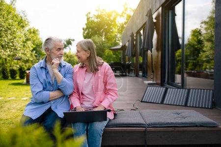 Photo for Senior man and woman sitting on house porch with solar panel using notebook. - Royalty Free Image