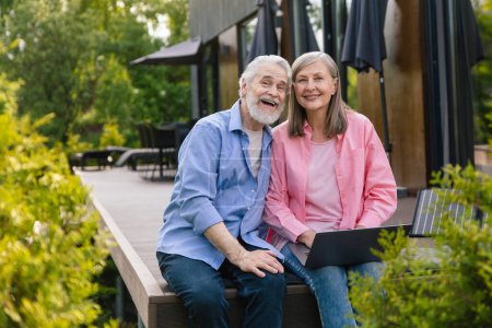 Foto de Hombre y mujer mayores sentados en el porche de la casa con panel solar usando portátil. - Imagen libre de derechos