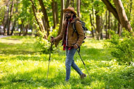 Téléchargez les photos : Randonnée. Jeune homme en randonnée dans la forêt avec des bâtons scandinaves - en image libre de droit