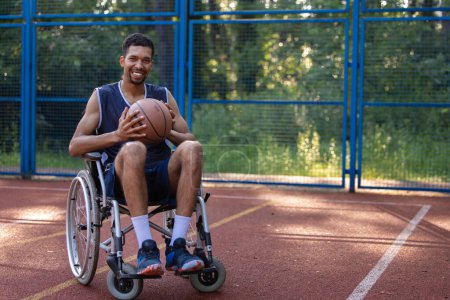 Téléchargez les photos : Heureux joueur de basket-ball avec handicap utilise fauteuil roulant tout en jouant sur le terrain de sport extérieur. - en image libre de droit