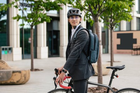 Photo for Way to the office. Man in hemlet on a bike in the office area - Royalty Free Image