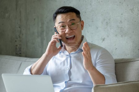 Téléchargez les photos : Homme heureux entrepreneur travaillant assis sur un canapé travaillant sur un ordinateur portable et parlant téléphone mobile. - en image libre de droit