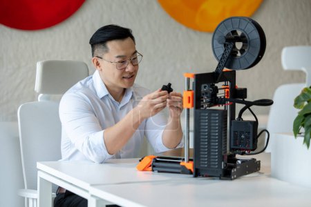 Téléchargez les photos : Concepteur masculin asiatique utilisant une imprimante 3D au bureau, travaillant avec de nouvelles idées technologiques. - en image libre de droit