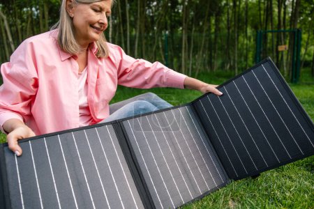 Foto de Mujer de mediana edad con panel solar portátil en el patio. - Imagen libre de derechos