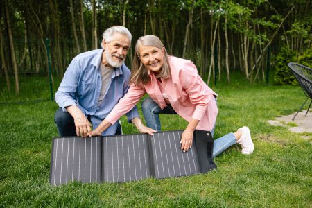 Téléchargez les photos : Homme et femme souriants montrant chargeur solaire, batterie d'alimentation, panneau solaire flexible. - en image libre de droit