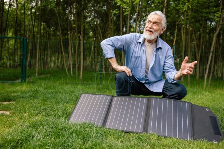 Foto de Hombre mayor de pelo gris sosteniendo el panel solar en el patio verde. - Imagen libre de derechos
