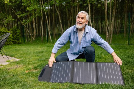 Photo for Bearded mature man holding solar panel in garden. - Royalty Free Image