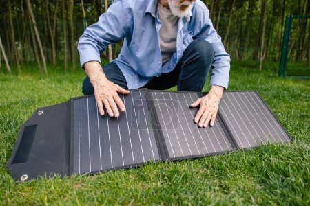 Photo for Unrecognizable senior man holding solar panel on in green yard. - Royalty Free Image