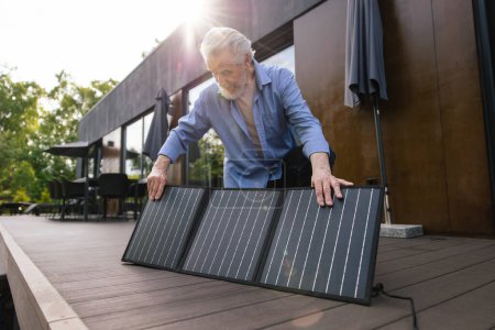 Téléchargez les photos : Homme caucasien avec panneau solaire technologie d'innovation énergie alternative sur le porche de la maison. - en image libre de droit