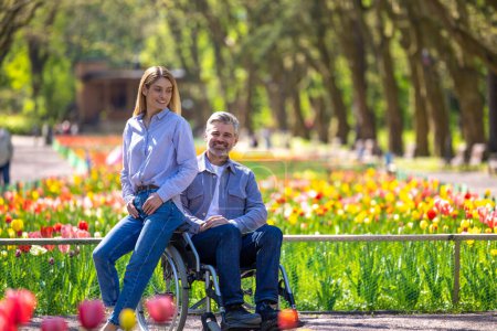 Photo for Disabled man in wheelchair with wife walking in park. - Royalty Free Image