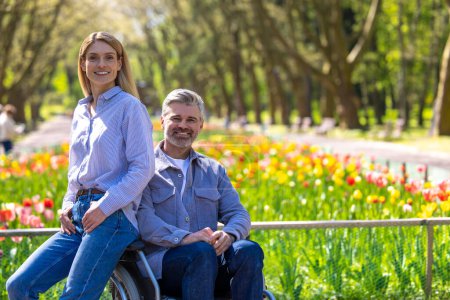 Téléchargez les photos : Femme d'âge moyen romantique et homme handicapé en fauteuil roulant marchant dans le parc, marche romantique. - en image libre de droit