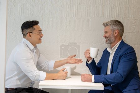 Foto de Dos hombres de negocios toman un descanso tomando café y discutiendo la estrategia de negocios en la oficina. - Imagen libre de derechos