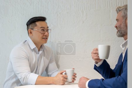 Téléchargez les photos : Deux hommes d'affaires prennent une pause en buvant du café et en discutant de stratégie commerciale au bureau. - en image libre de droit