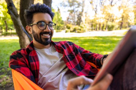 Photo for Peaceful mood. Dark-haired young bearded man in checkered shirt lying in hammock - Royalty Free Image