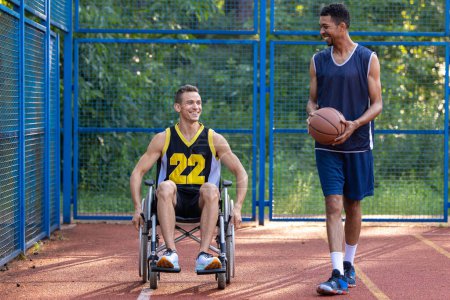 Foto de Caucásico hombre en silla de ruedas jugando baloncesto con un amigo en la cancha al aire libre. - Imagen libre de derechos