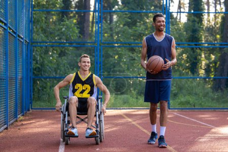 Foto de Caucásico hombre en silla de ruedas jugando baloncesto con un amigo en la cancha al aire libre. - Imagen libre de derechos