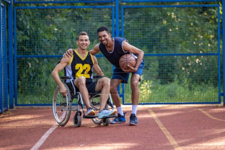 Photo for Man playing basketball with disabled friend in wheelchair at outdoor court. - Royalty Free Image