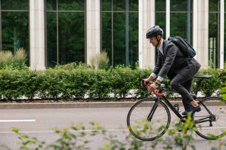 Photo for Way to work. Man in hemlet and with a backpack riding a bike - Royalty Free Image