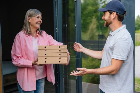 Téléchargez les photos : Livrer homme boîte de manutention de pizza donner à femme costumer en face de la maison. - en image libre de droit
