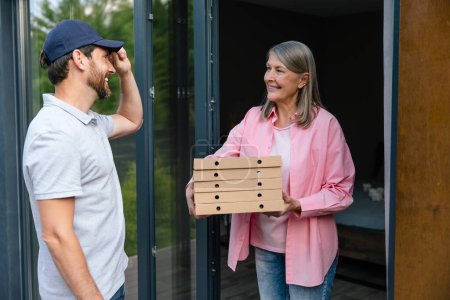 Photo for Courier man handling pizza to female client in front of the house. - Royalty Free Image