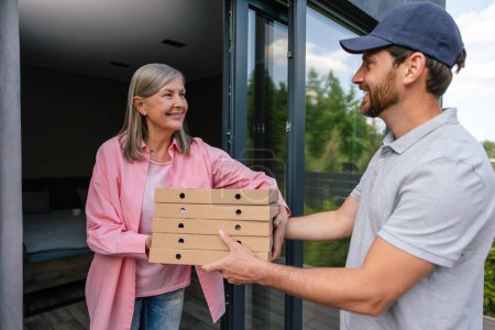 Photo for Deliver man handling box of pizza give to female costumer in front of house. - Royalty Free Image