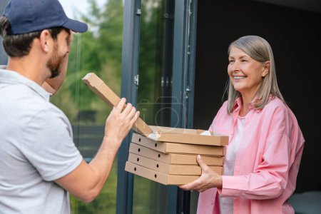 Photo for Deliver man handling box of pizza give to female costumer in front of house. - Royalty Free Image