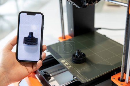 Foto de Hombre irreconocible sosteniendo el teléfono inteligente con detalle en la pantalla, trabajando en la impresora 3D en el laboratorio creativo. - Imagen libre de derechos