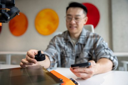 Téléchargez les photos : Asiatique brun homme concepteur tenant deteil imprimé sur imprimante 3D travaillant dans l'atelier d'ingénierie. - en image libre de droit
