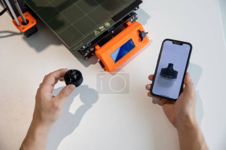 Foto de Hombre irreconocible sosteniendo el teléfono inteligente con detalle en la pantalla y haciendo en la impresora 3D en el laboratorio creativo. - Imagen libre de derechos